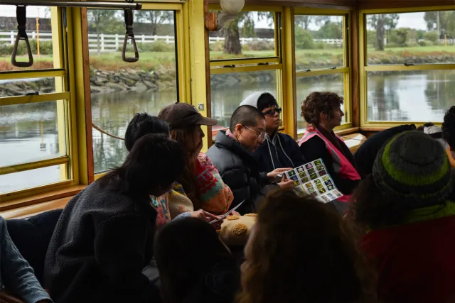 Event participants sitting and listening along the window seat of the Tramboat